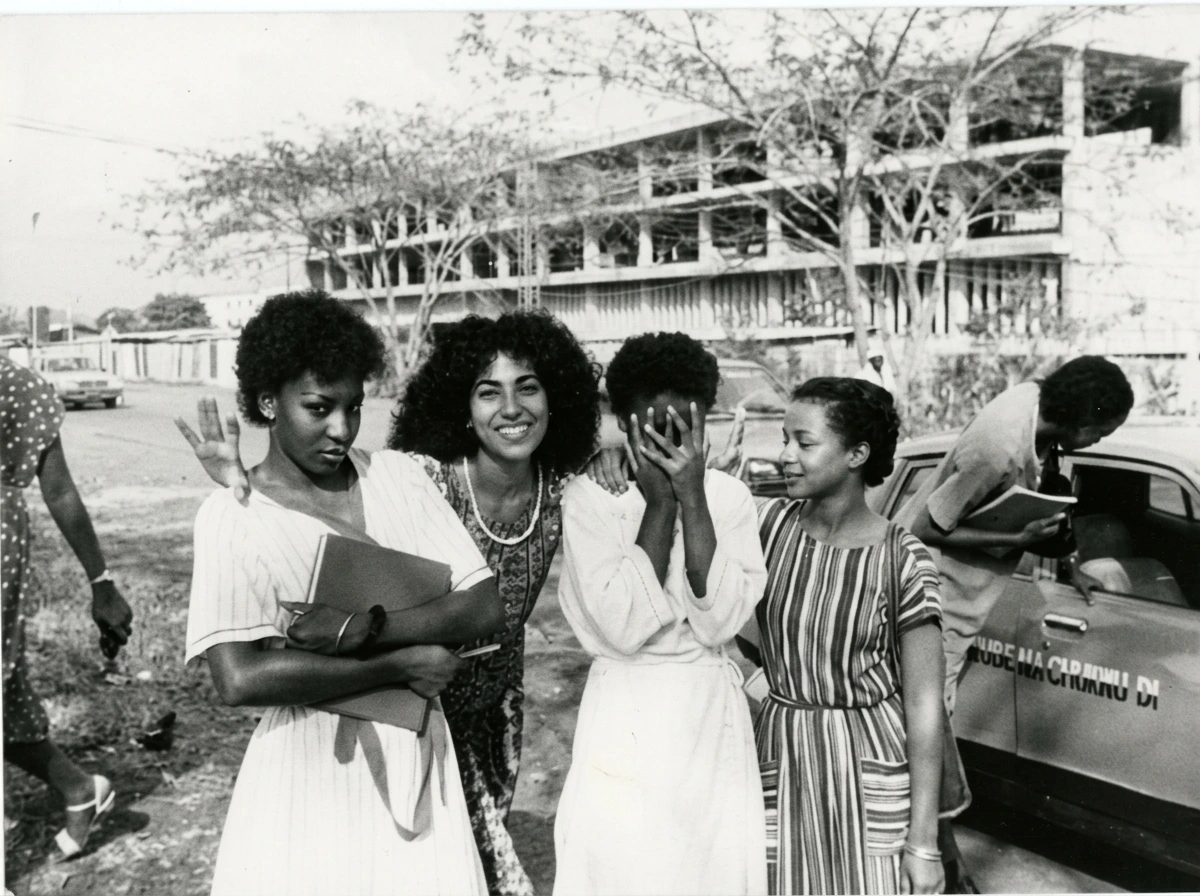 Portrait of young Nigerian university women posing beside a car in mid-century Lagos.