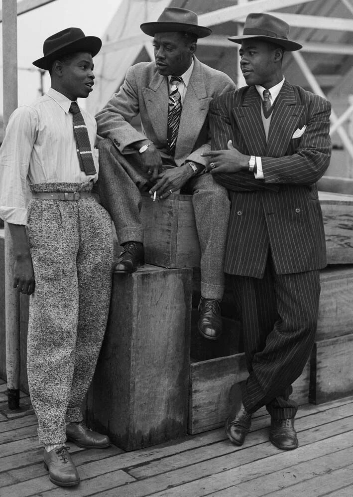 Archival portrait of three stylishly dressed Nigerian men in tailored suits and fedoras, post-war era.